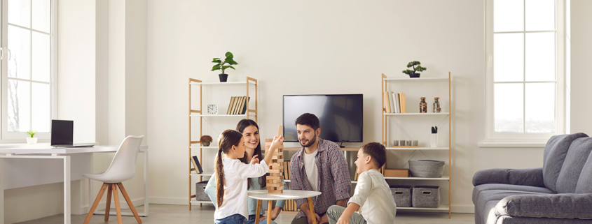 Family room trends for 2022 - Happy family father mother and two children sitting on floor and playing at home together during weekend. Family spending happy time at home and having fun with children concept