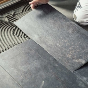 Worker placing dark grey ceramic floor tiles on adhesive surface